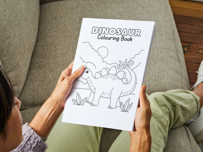 Person holding a dinosaur coloring book on a couch