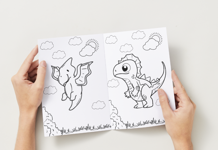 Coloring book with dinosaur illustrations held by hands on a light background