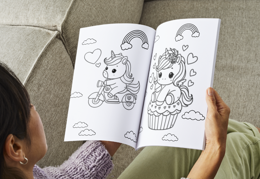 Person holding a coloring book with unicorn illustrations on a couch.